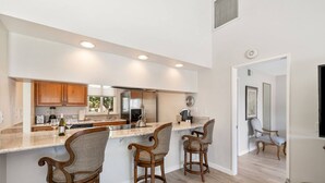A modern kitchen with a large island, wooden bar stools, and stainless steel appliances.