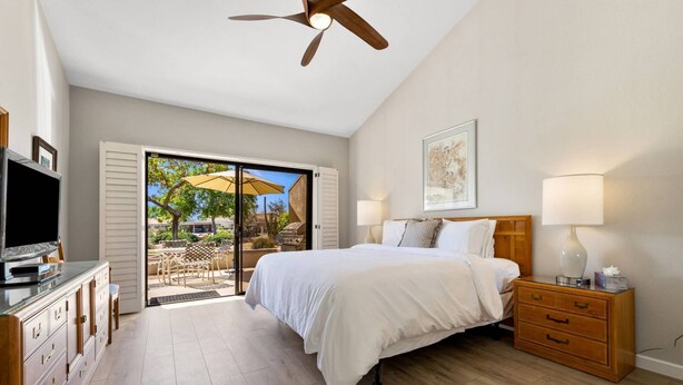 A bedroom with a bed, a TV, a wooden dresser, a nightstand, and a ceiling fan.