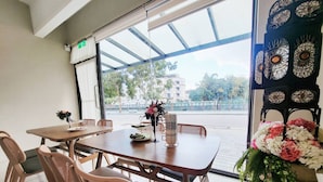 A dining area with a table and chairs, a flower arrangement, and a view of the street outside. - Near River Homestay (Ji'an)