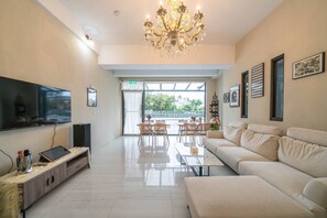 A modern living room with a flat-screen TV, a sofa, a coffee table, and a chandelier.