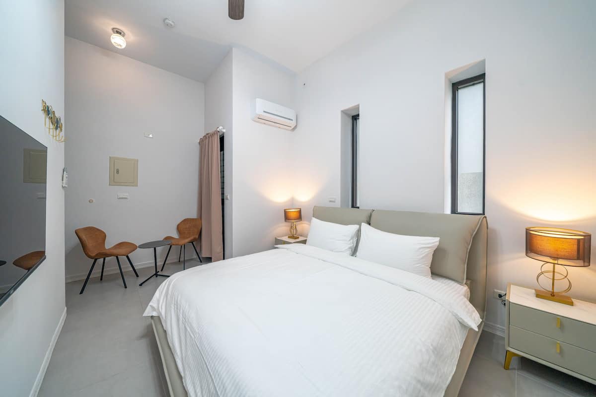 Una habitación de hotel con una cama grande, mesitas de noche, un escritorio con sillas y un aire acondicionado.