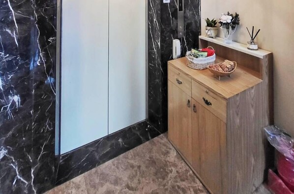 A modern bathroom with a marble wall, a wooden vanity with a basket and a small plant, and a trash bin.