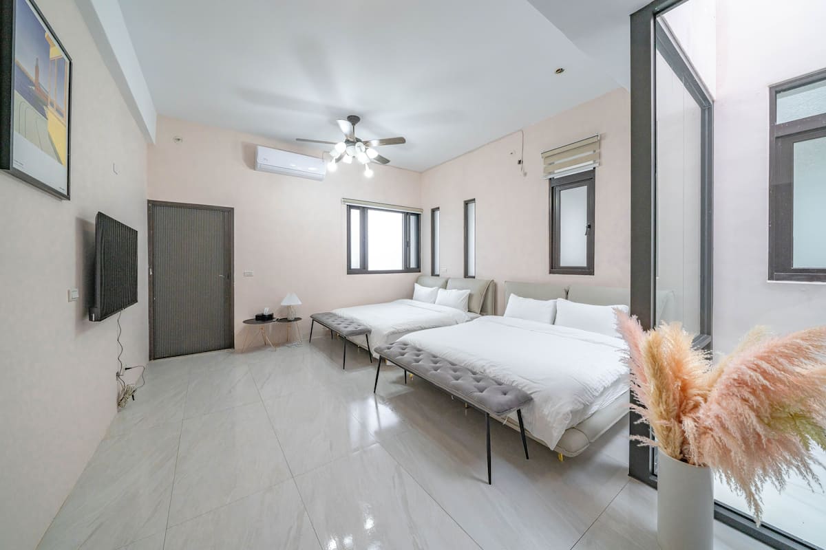 Un dormitorio moderno con dos camas, un ventilador de techo y un ventanal grande.
