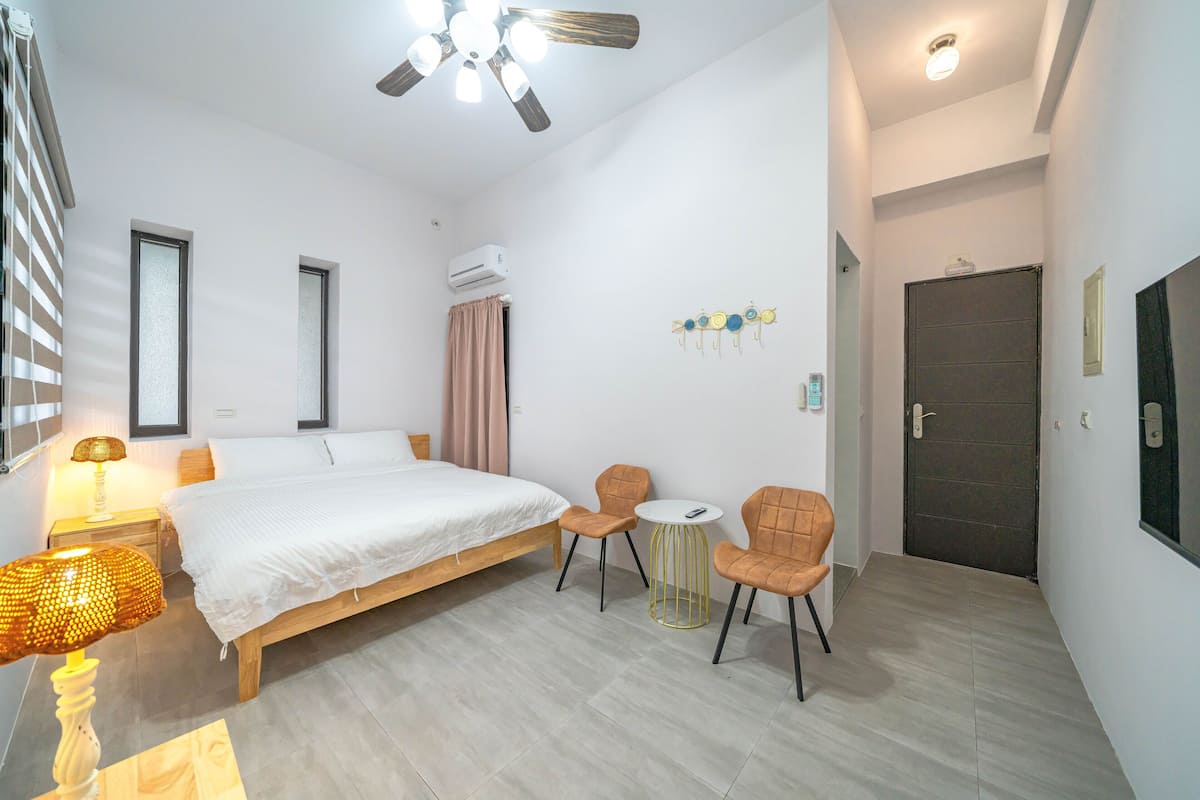 Un dormitorio con una cama, mesitas de noche, una lámpara, un ventilador de techo y una pequeña mesa redonda con sillas.