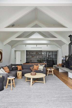 A spacious living area with a high ceiling, a sectional sofa, a coffee table, and a fireplace.