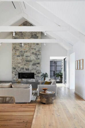 A spacious living room with a stone fireplace, a sofa, a coffee table, and a wooden dining table.
