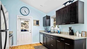 A modern kitchen with dark cabinets, a granite countertop, a sink, and a clock on the wall. - Fantastic Rockaway Family Escape – Close to Beach with BBQ (Rockaway Beach)