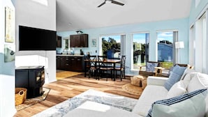 A spacious living room with a fireplace, a dining area with a large table and chairs, and a kitchen with dark cabinets and a window. - Fantastic Rockaway Family Escape – Close to Beach with BBQ (Rockaway Beach)