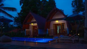 Two wooden chalets with tiled roofs, a swimming pool, and lounge chairs.