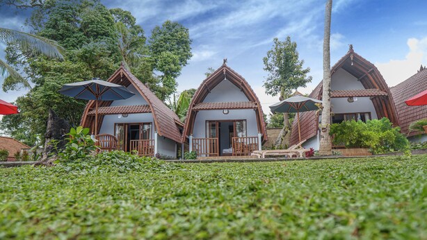 A row of traditional-style villas with thatched roofs, wooden balconies, and a lush garden in the foreground.