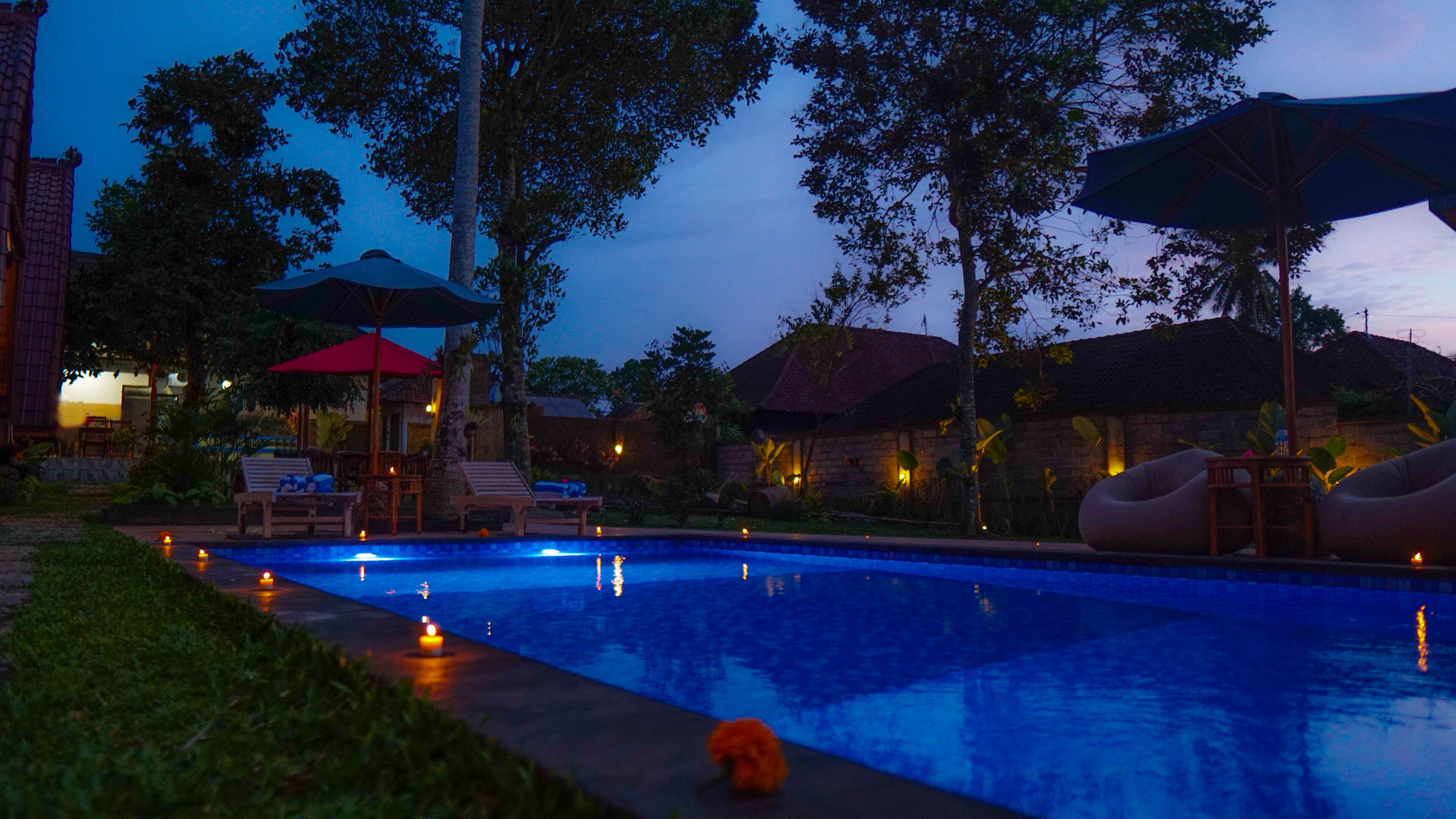A swimming pool area with lounge chairs, umbrellas, and a slide, surrounded by trees and buildings.