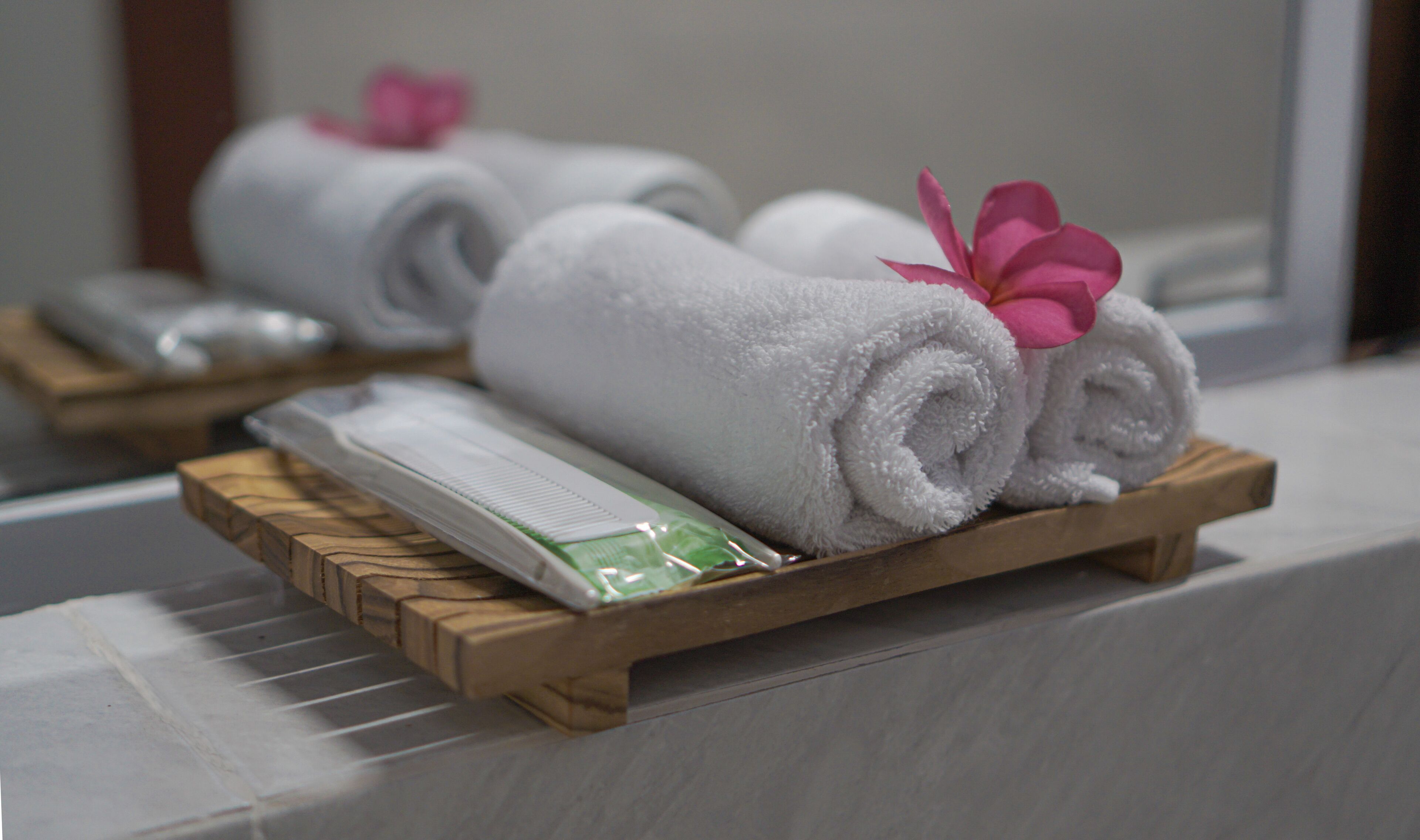 Neatly rolled white towels with pink flowers on a wooden tray in a bathroom.