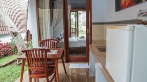 A small, cozy room with a wooden dining table and chairs, a bed with a white mattress, and a kitchen area with a sink and a refrigerator.