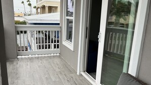 Ein Balkon mit einer grauen Couch, einem weißen Geländer und Blick auf ein Gebäude mit Balkon.