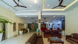 A spacious living room with a brown sofa, a wooden coffee table, and multiple ceiling fans. - Starlite Hotels (Vanur)