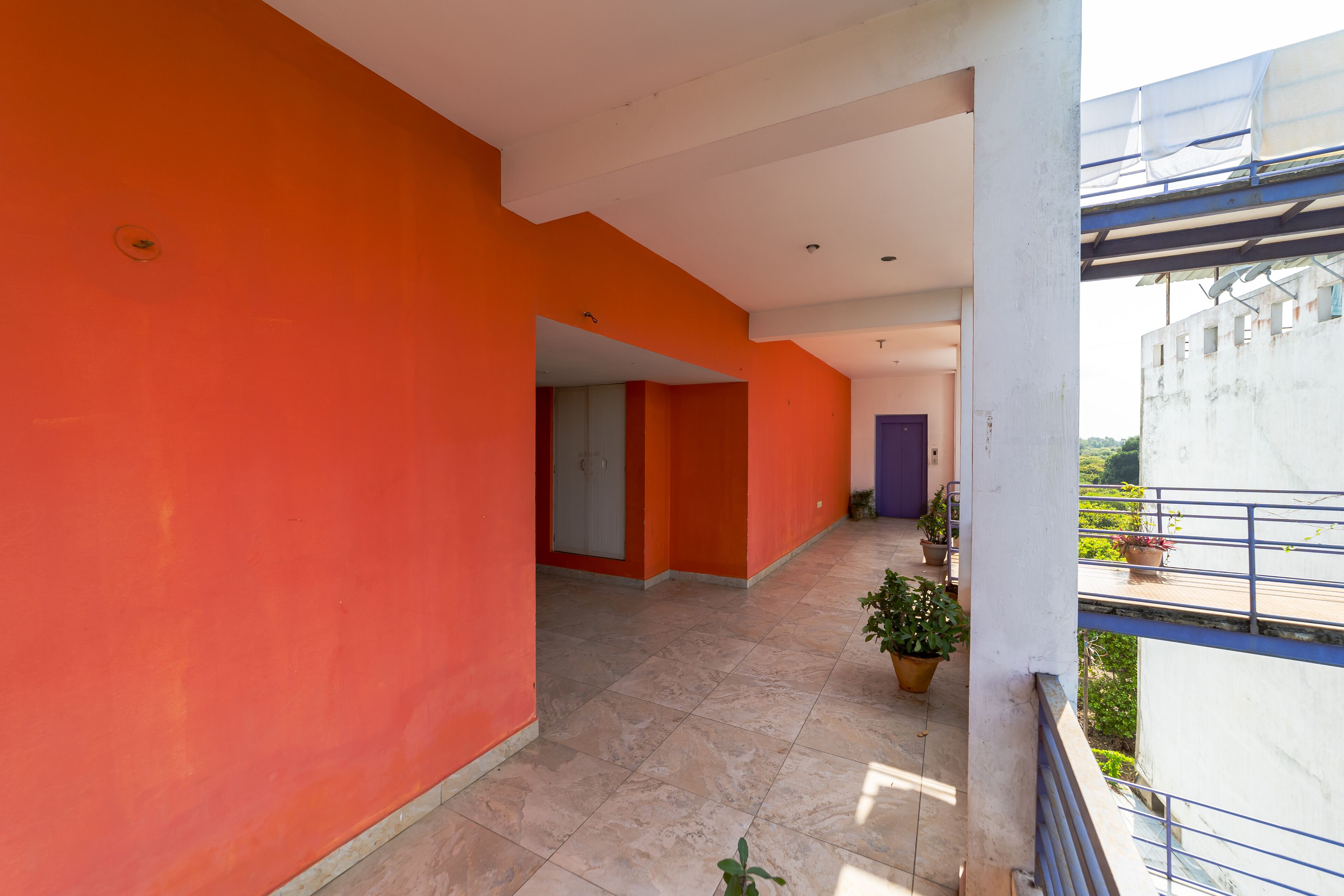 A corridor with orange walls and a tiled floor, leading to a door with a purple frame.
