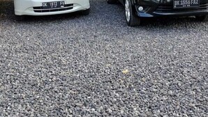 Deux voitures garées sur une allée de gravier, entourées de verdure et bordée d’un mur de pierres.