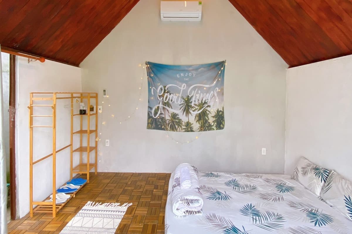 A cozy attic bedroom with a sloped ceiling, a bed with a tropical leaf pattern, a wooden bunk bed, and a hammock.