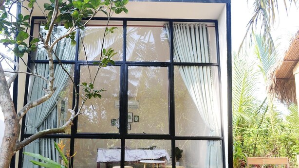 A modern building with large windows, a small table with a white tablecloth, and a bench outside. - Hide Away Homestay (Phu Khuong)