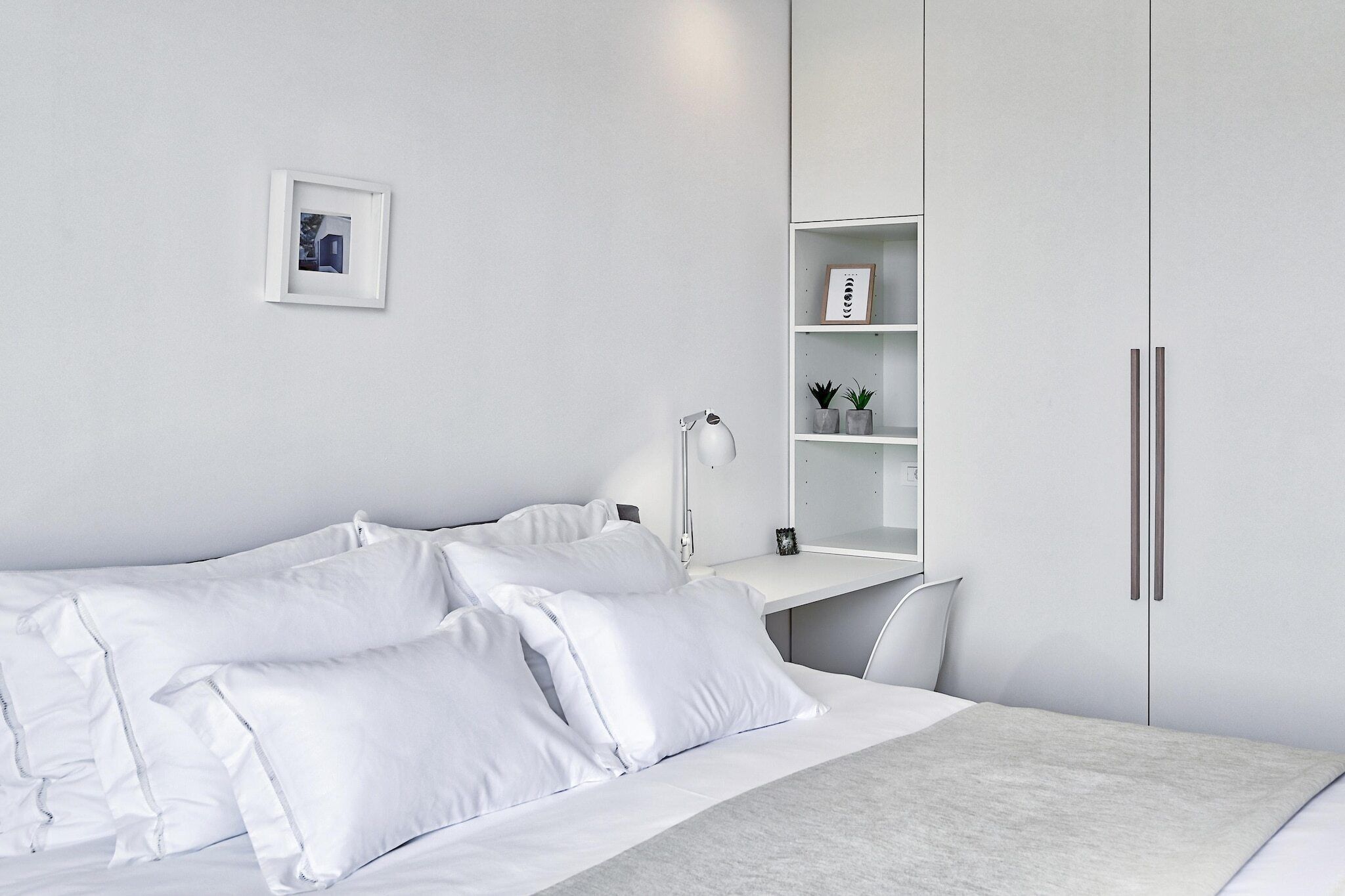 A minimalist bedroom with a bed, bedside table, lamp, and a wardrobe.