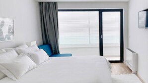 A modern bedroom with a large bed, a blue chair, and a sliding glass door leading to a balcony.