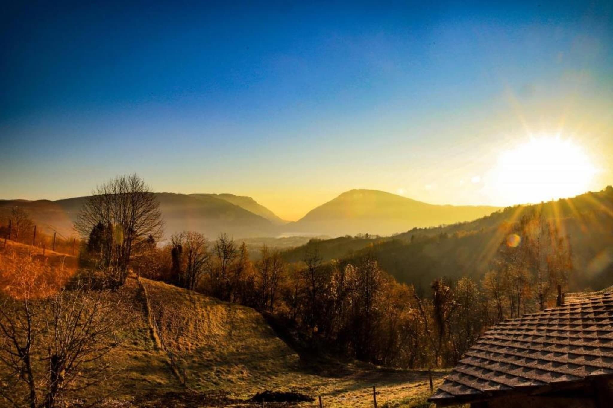 Un paysage rural avec une maison située sur une colline, entourée d’arbres et de collines.