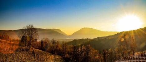 Un paysage rural avec une maison située sur une colline, entourée d’arbres et de collines.