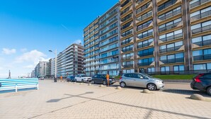 Ein modernes Mehrfamilienhaus mit mehreren Etagen, einem gepflasterten Weg und geparkten Autos.