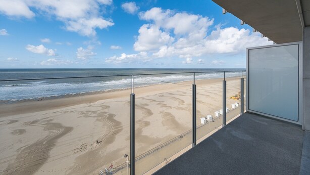 Ein Balkon mit Blick auf einen Sandstrand und das Meer unter blauem Himmel.