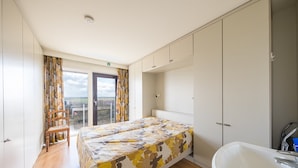 Ein Schlafzimmer mit Bett, ein Badezimmer mit Waschbecken und Blick ins Freie.