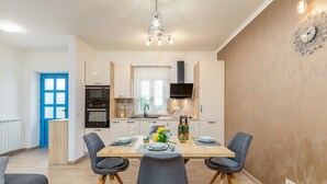 A modern kitchen with a dining area, featuring a wooden table, grey chairs, and a hanging light fixture.