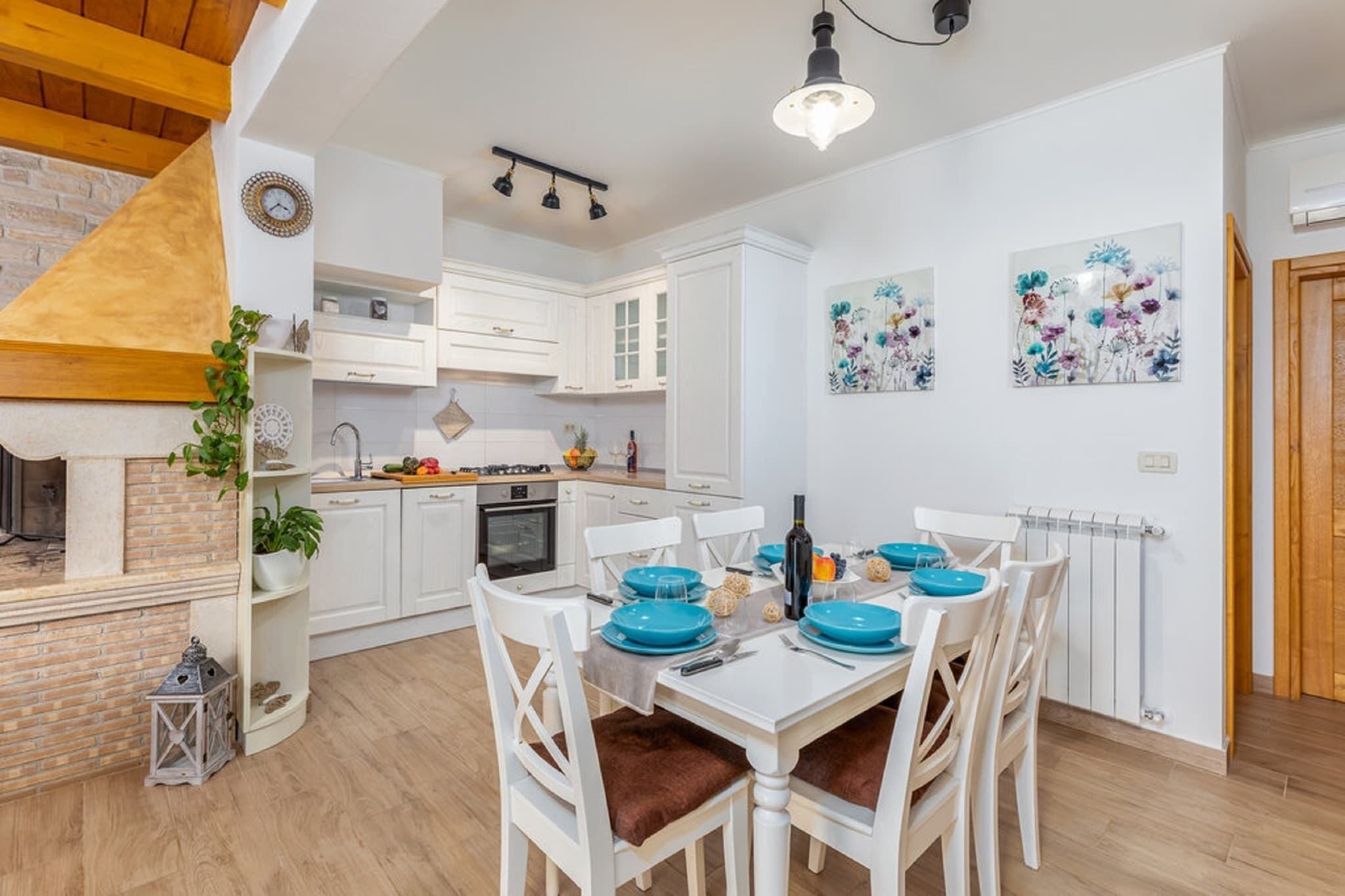 Une cuisine moderne avec des meubles blancs, une table à manger dressée avec de l’assiette bleue et une cheminée en briques.
