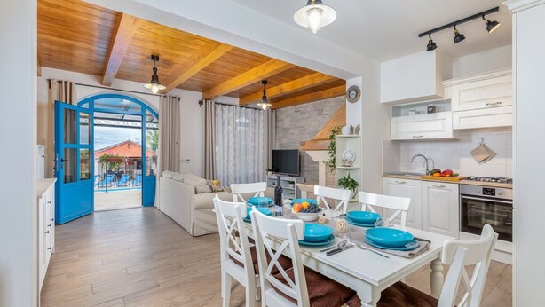 A modern kitchen with white cabinets, a dining area with white chairs and blue plates, and a wooden ceiling.