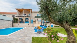 A house with a swimming pool, a covered patio, and a garden with flowers.