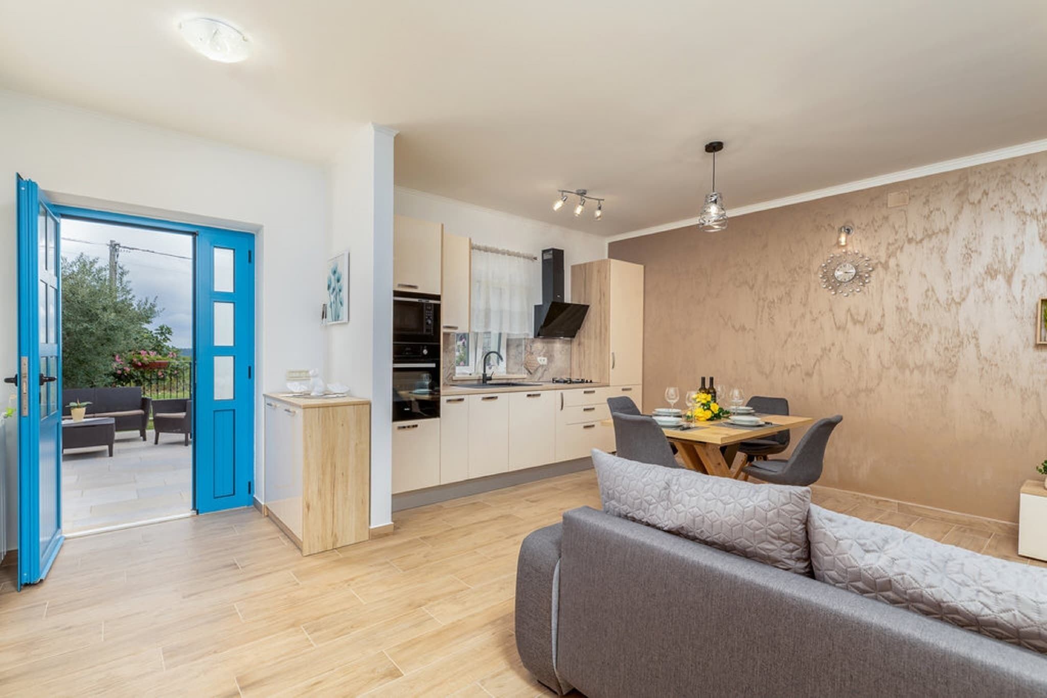 A modern kitchen with a dining area, a sofa, and a blue door leading to an outdoor seating area.