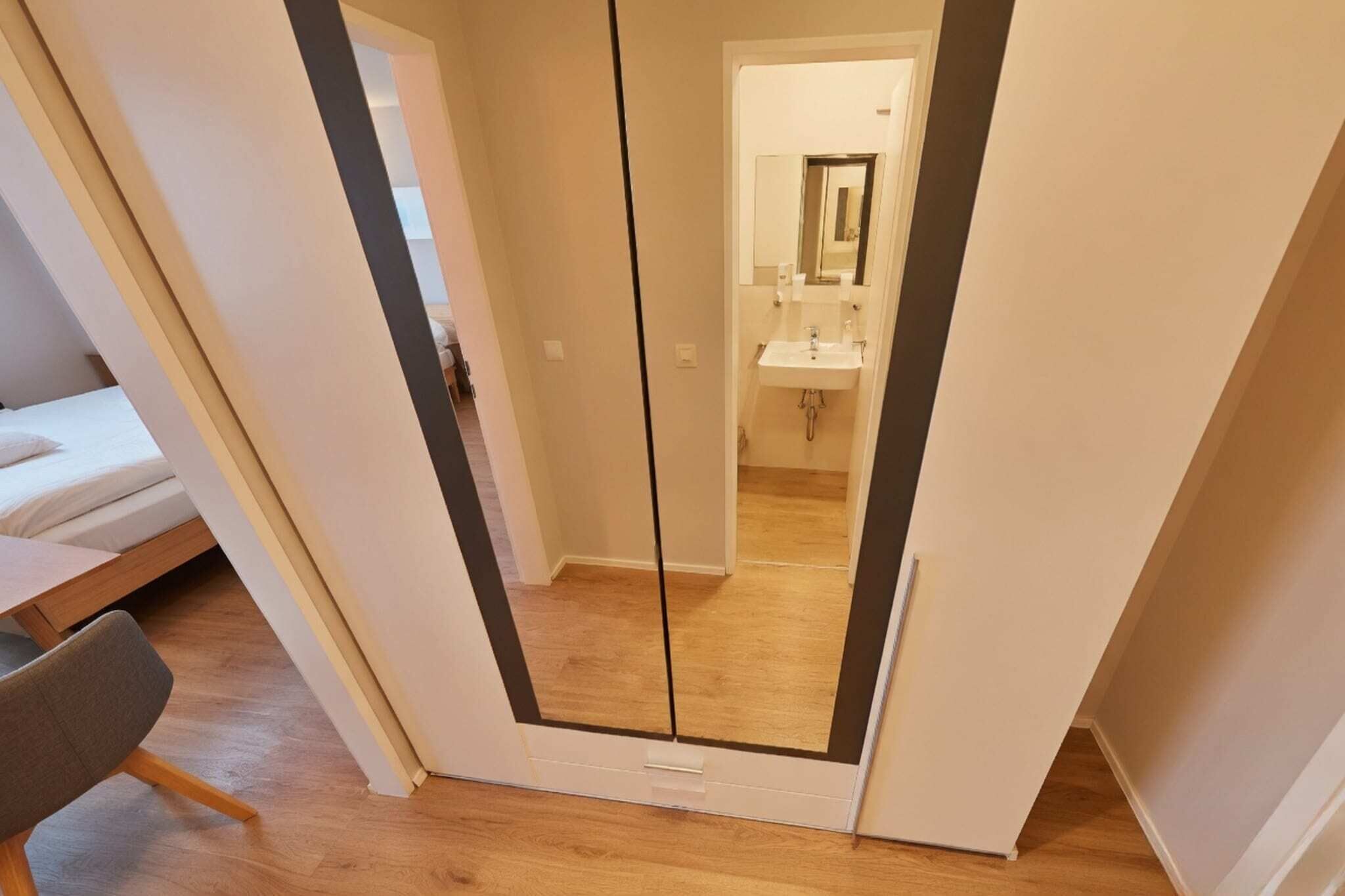 A bedroom with a bed, a chair, and a mirror.