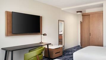 A hotel room with a bed, a desk with a chair, a flat-screen TV, a mirror, and a wardrobe.
