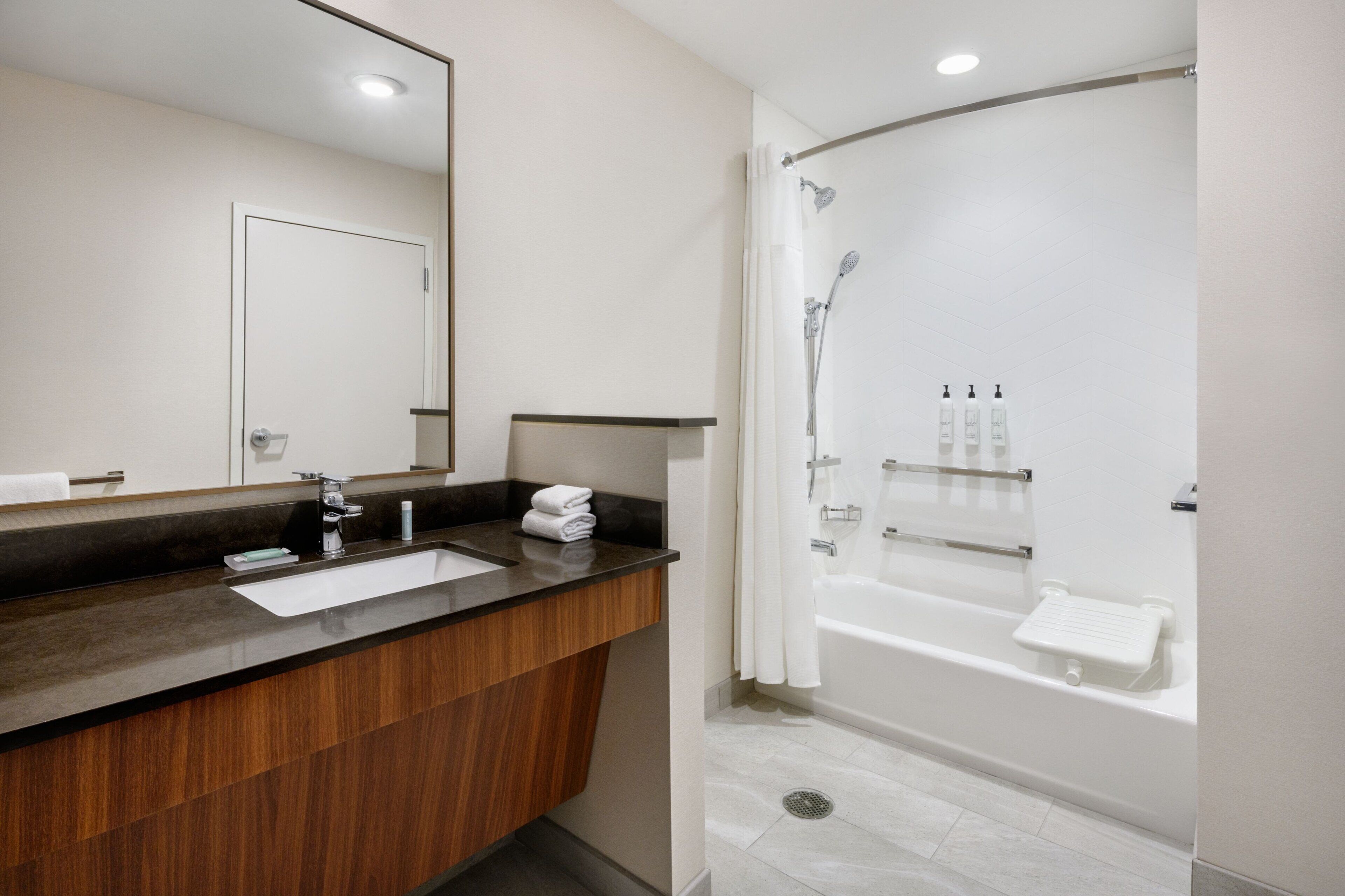 Un baño moderno con tocador de madera, un espejo grande, una bañera y una ducha.