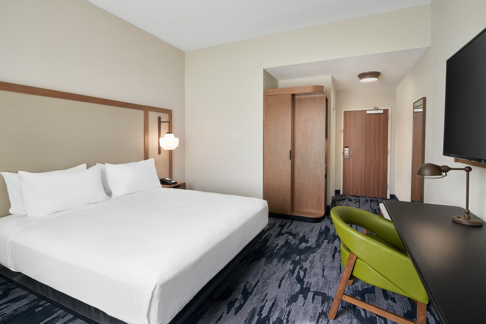 A hotel room with a bed, a desk, a chair, a television, and a wardrobe.