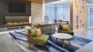 A modern living room with a fireplace, comfortable seating, a dining area, and large windows. - NEW - Fairfield Inn & Suites by Marriott Orlando at Millenia (Orlando)