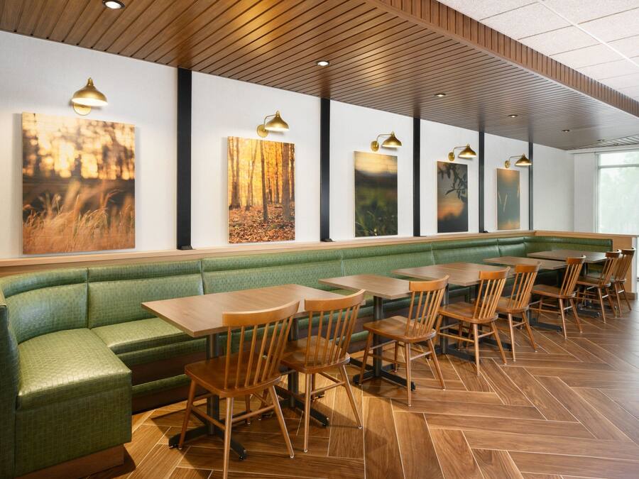 Un restaurante con un área de asientos en una cabina verde, mesas y sillas de madera.