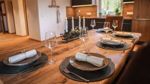 A wooden dining table set with plates, glasses, and cutlery, candles, and a decorative centerpiece.