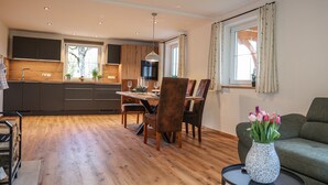 A modern kitchen with wooden cabinets, a dining area with a table and chairs, and a living room with a sofa and a vase of flowers.