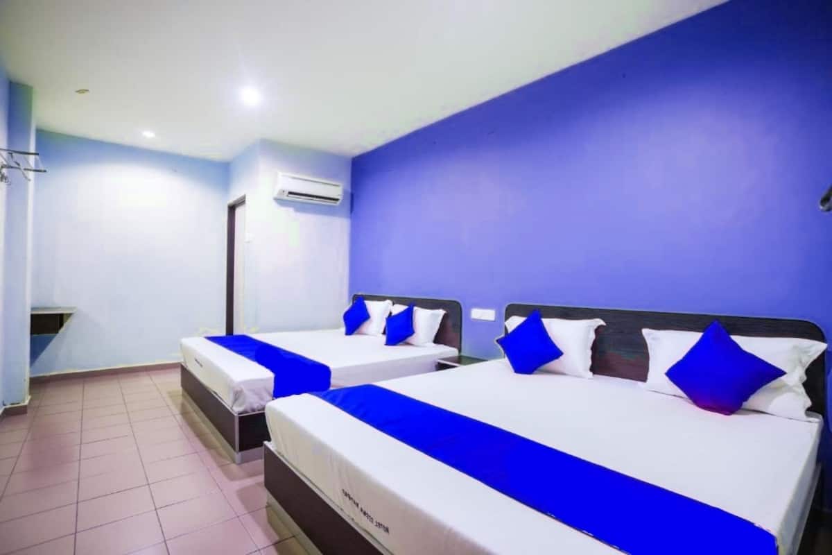 Habitación de hotel con dos camas, cada una con cubrecama azul y almohadas blancas.