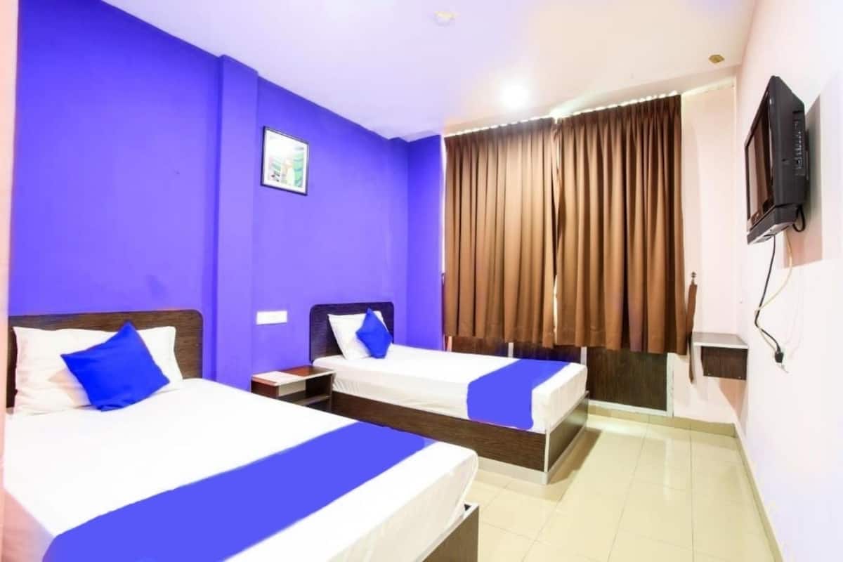 Habitación de hotel con dos camas, un televisor montado en la pared y una ventana con cortinas.