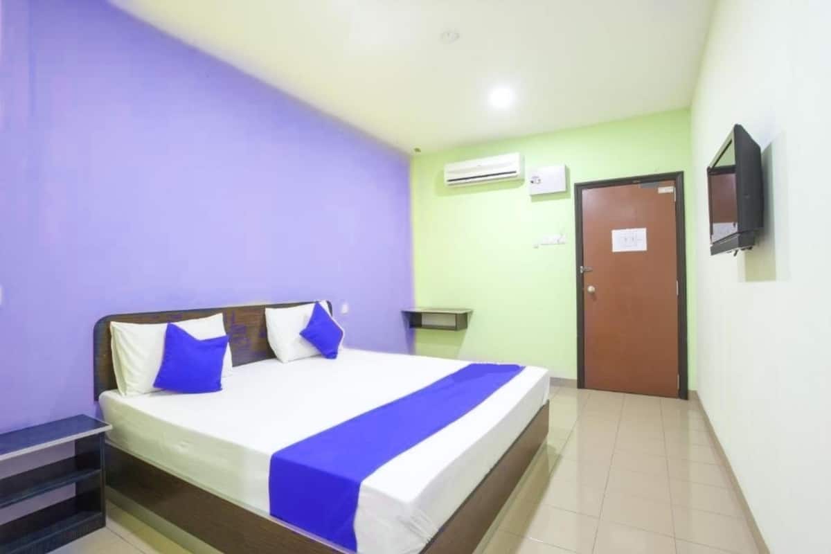 Una habitación de hotel con cama, televisor montado en la pared, aire acondicionado y puerta.