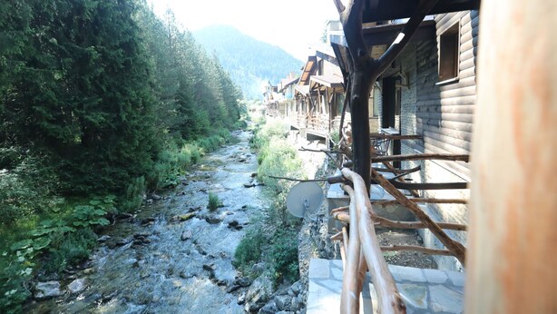 A wooden cabin with a stone foundation, a wooden deck, and a view of a river and forest. - Holiday village Horlog Castle (Devin)