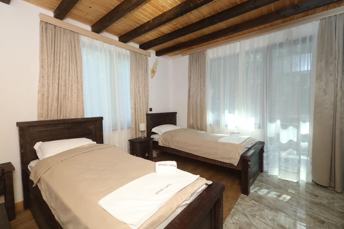 A hotel room with two wooden beds, beige bedding, and a wooden ceiling.