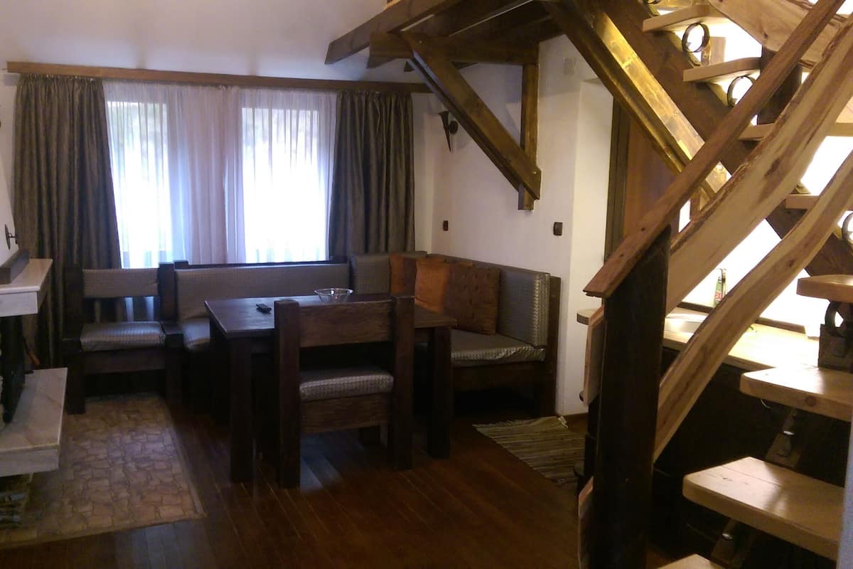 A cozy room with a stone fireplace, wooden furniture, and a staircase.