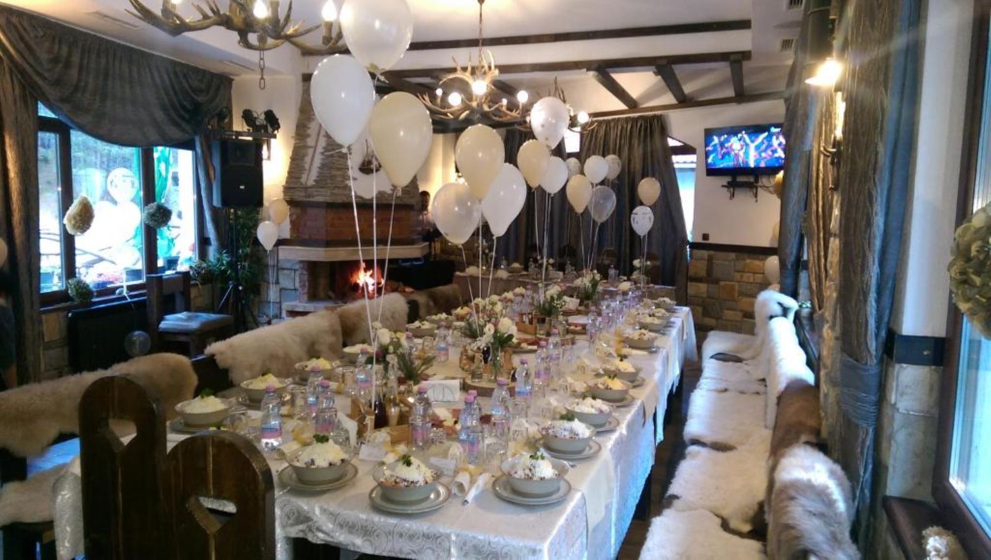 Een lange eettafel gedekt voor een formeel evenement, met witte tafelkleden, bloemstukken als middelpunt en ballonnen.